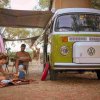 Famiglia in campeggio accanto a un furgone Volkswagen verde, coperta colorata e telo ombreggiante.