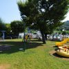 Parco giochi con scivolo giallo e altalene, circondato da alberi.