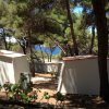Campeggio tra alberi con vista sul mare, piccole strutture bianche e fiori.