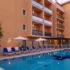 Piscina di fronte a un edificio color pesca con lettini e ombrelloni.