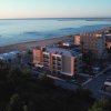 Vista aerea di edifici costieri vicino alla spiaggia al tramonto, con il mare calmo sullo sfondo.