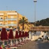 Ombrelloni chiusi su una spiaggia sabbiosa, edificio giallo sullo sfondo.