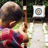 Un bambino con arco e freccia mira a un bersaglio colorato in un giardino.