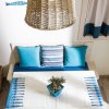 Tavolino con centrino bianco e blu, cuscini coordinati su una panca, lampadario di vimini.