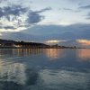 Tramonto su un lungomare con luci riflettenti sull'acqua, cielo nuvoloso.