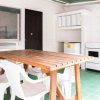 Cucina all'aperto con tavolo in legno, sedie bianche, frigorifero e lavello su pavimento verde.