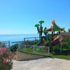 Parco giochi colorato con scivoli, vicino al mare e circondato da aiuole di fiori rosa.