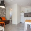 Soggiorno moderno con divano marrone, cuscini colorati, cucina bianca e tavolino con fiori.