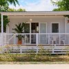 Casa mobile bianca con veranda, sedie e pianta in vaso davanti.