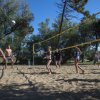 Persone giocano a beach volley su un campo sabbioso, circondato da alberi.